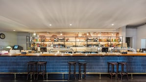 A bar area with a blue tiled counter, multiple stools, and a variety of bottles and glasses on shelves. - College Lawn Hotel - Hostel (Prahran)