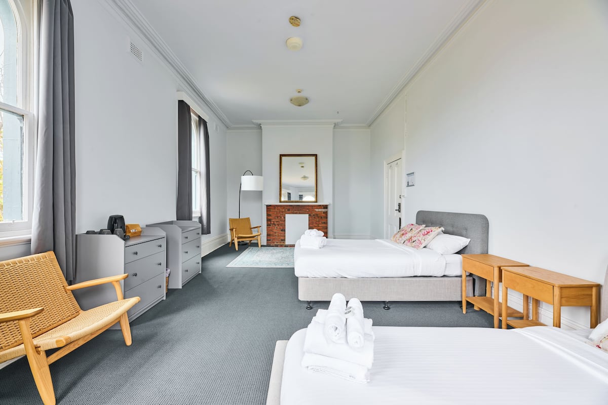 Habitación de hotel con dos camas, un sofá, un escritorio, una silla, una chimenea y un espejo grande.