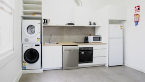 A compact kitchen with a washing machine, dishwasher, microwave, and refrigerator. - College Lawn Hotel - Hostel (Prahran)