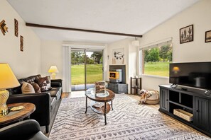 A living room with a sofa, a coffee table, a TV, a fireplace, and a view of the outdoors.