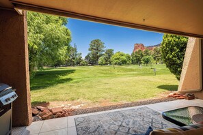 A patio with a grill, a view of a grassy area with trees, and a mountain in the background.