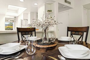 A dining table set with white plates, bowls, and glasses, a vase with branches, and a woven placemat.