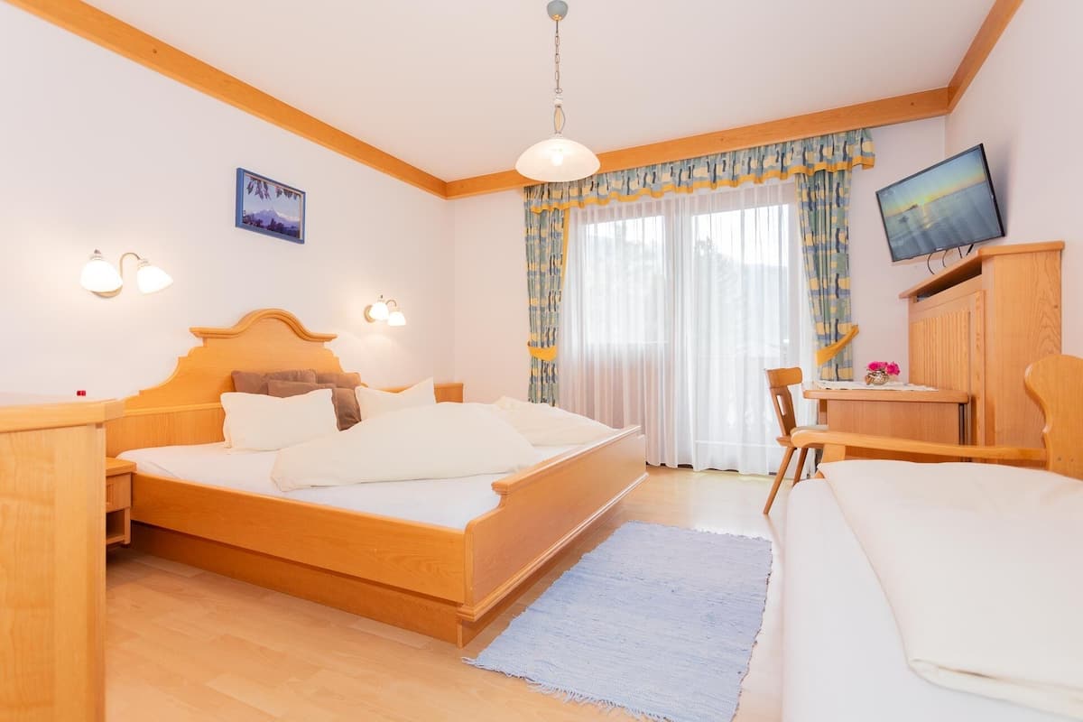 Une chambre à coucher avec un lit en bois, des tables de chevet, un bureau, une chaise, une télévision et une fenêtre avec des rideaux.