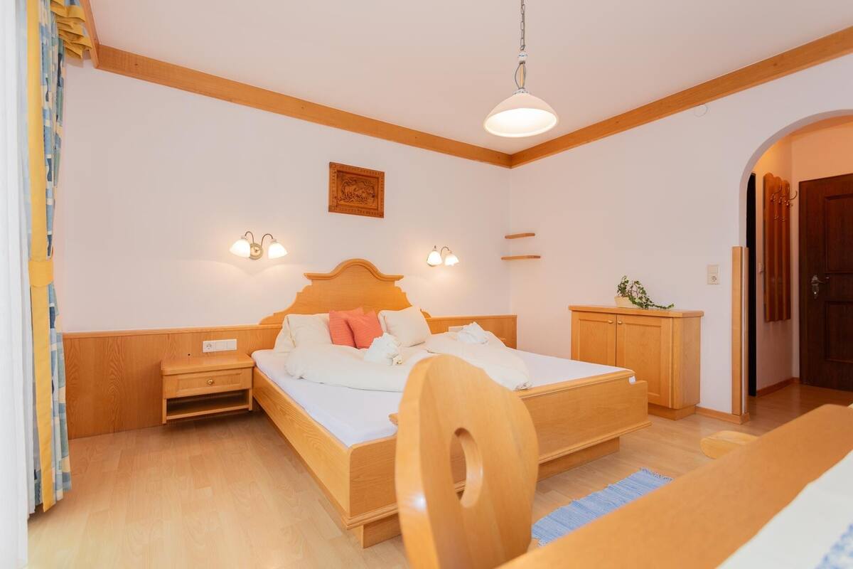 Une chambre à coucher avec un lit en bois, des tables de chevet, une petite table d’appoint, une armoire en bois et un luminaire suspendu.
