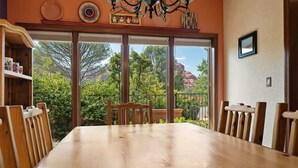 A dining area with a large wooden table, chairs, and large windows offering a view of trees and a mountain. - Home Surrounded by Lush Landscape + Mtn Views! (Sedona)