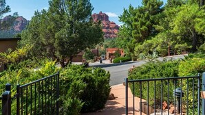 A residential area with a paved road, a metal fence, and a mountain in the background. - Home Surrounded by Lush Landscape + Mtn Views! (Sedona)
