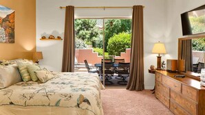 Une chambre à coucher comprenant un lit, une commode, un téléviseur et donnant sur une terrasse extérieure avec une table et des chaises.