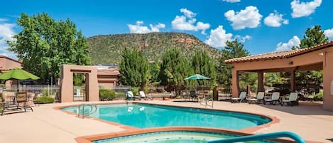 Piscina com espreguiçadeiras e guarda-sóis, rodeada por árvores e com uma montanha ao fundo.