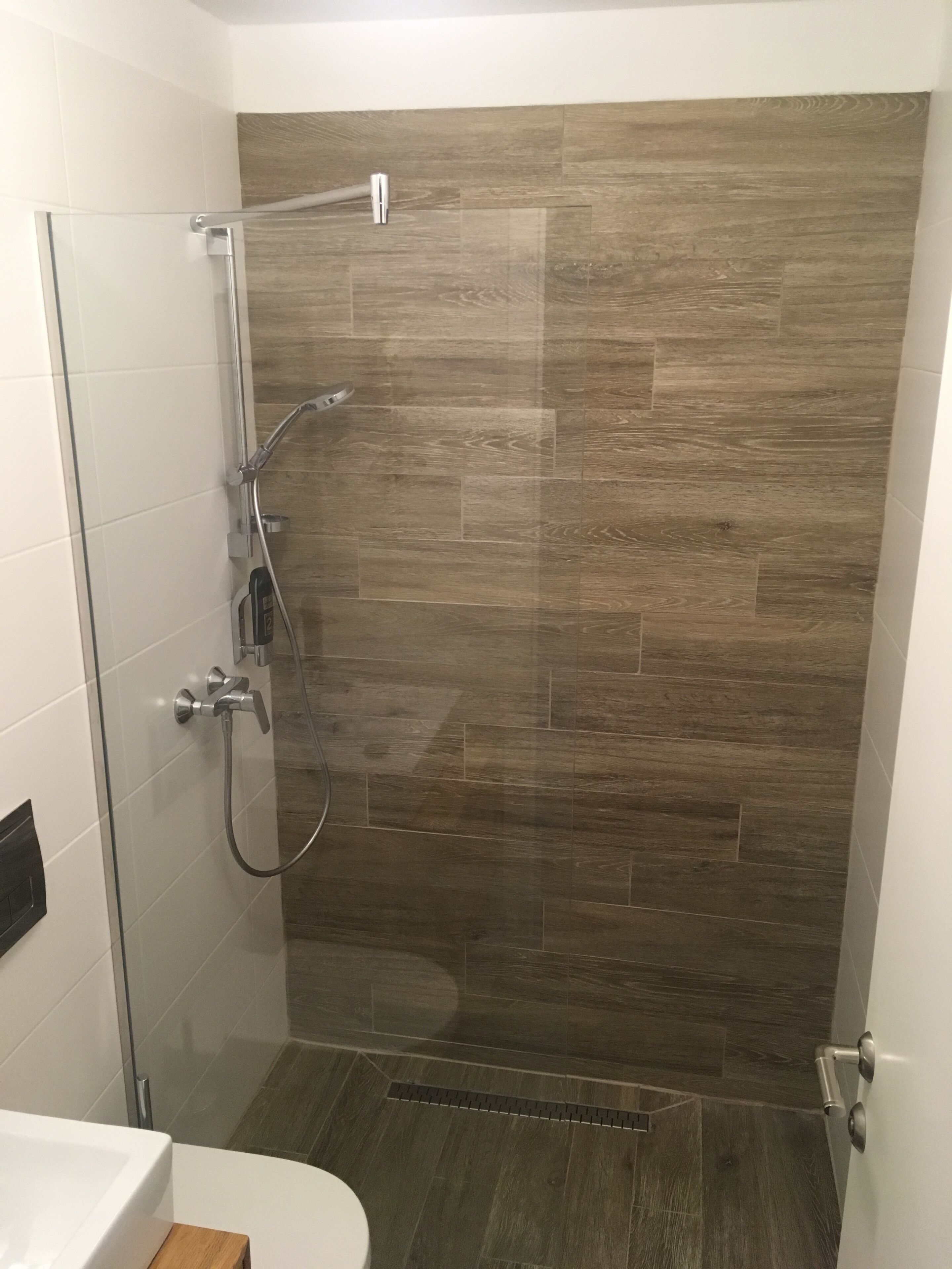 A modern bathroom with a glass shower enclosure, a white sink, and a wooden vanity.