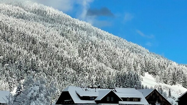 Une montagne enneigée sous un ciel dégagé. Au premier plan, on aperçoit des bâtiments aux toits inclinés, probablement un hôtel ou un chalet.