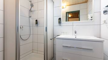 Un baño moderno con cabina de ducha de vidrio, un lavamanos blanco con un espejo encima y techo de madera.