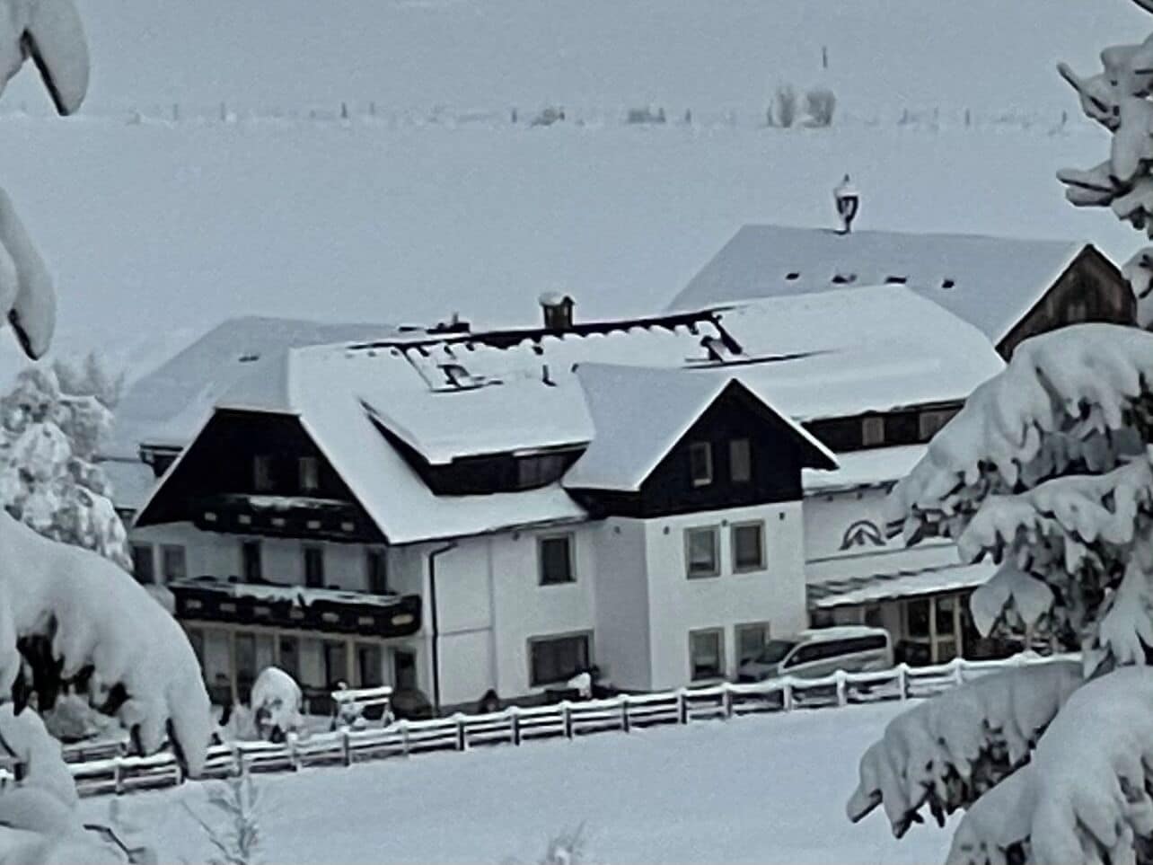 A multi-story building with a sloped roof, surrounded by snow-covered trees.