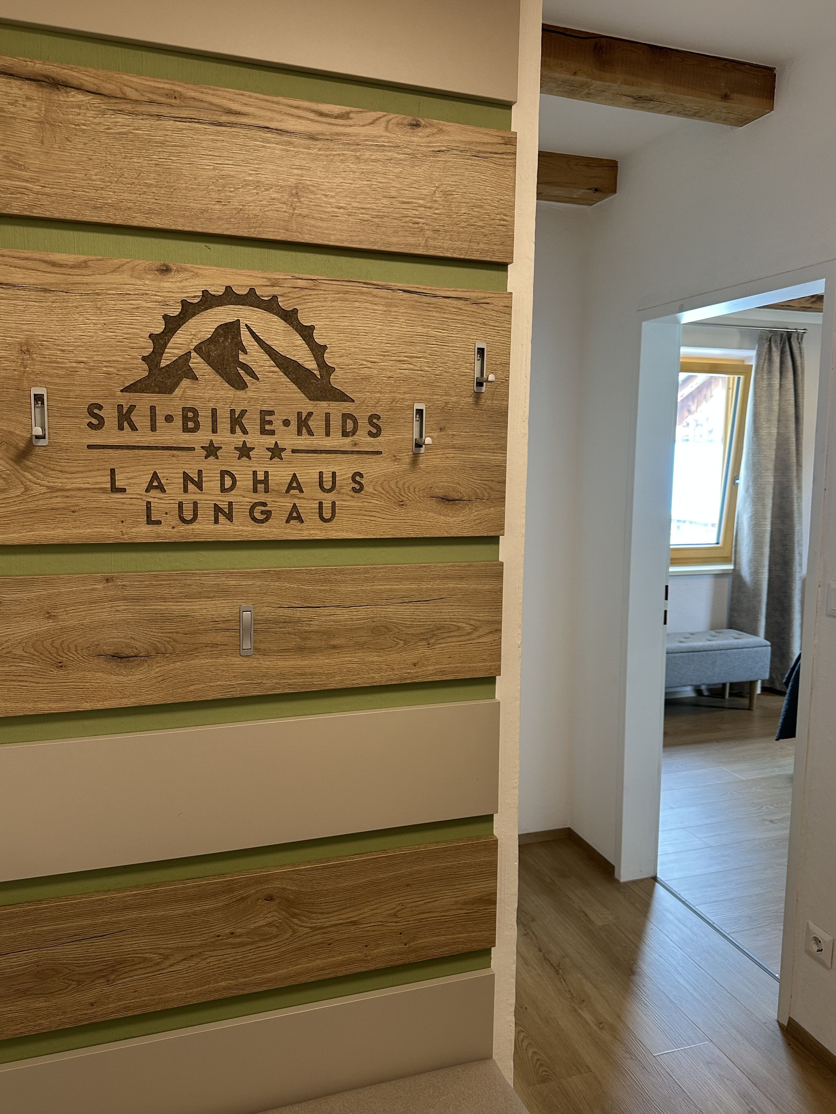 A wooden wall with the text "SKI-BIKE-KIDS LANDHAUS LUNGAU" and a mountain gear logo.