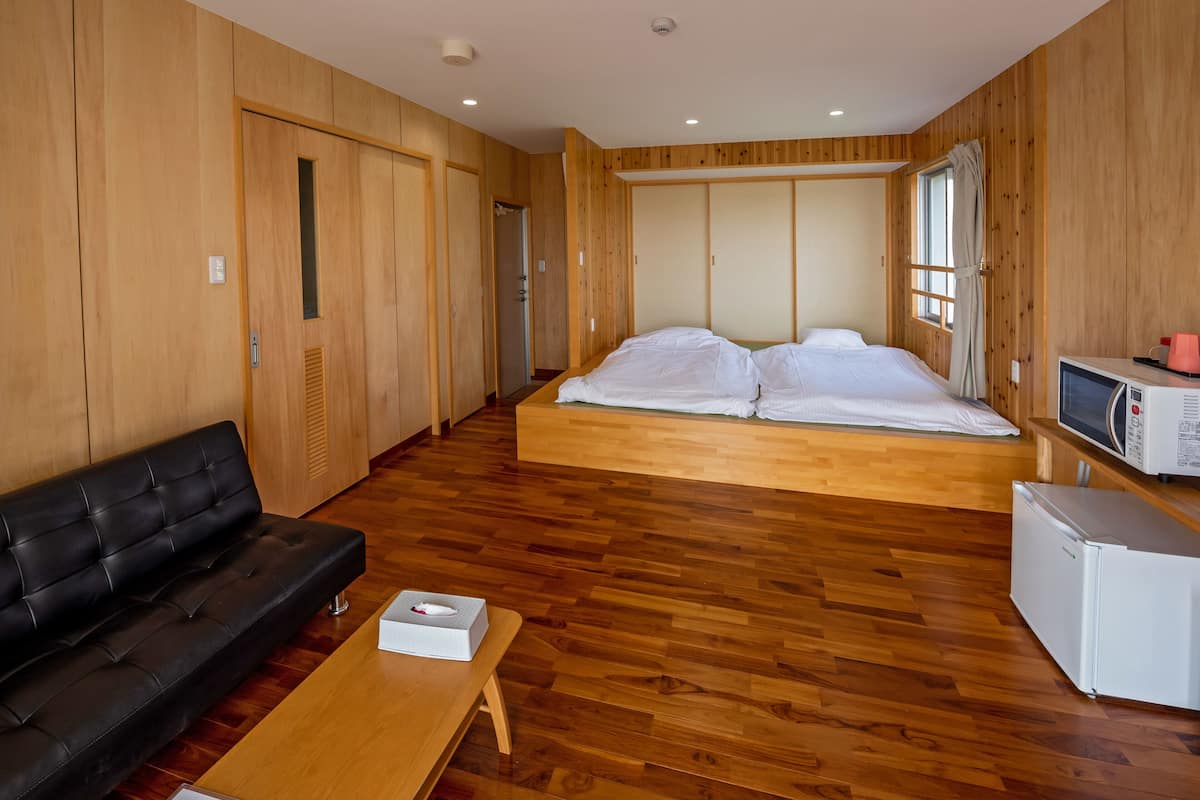 A room with a bed, a sofa, a small table, a microwave, and wooden paneling.