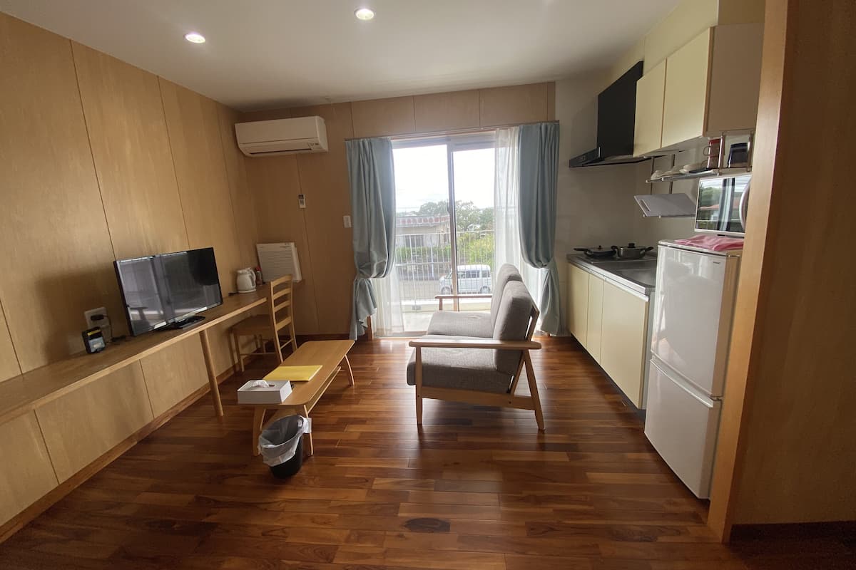 A modern apartment with a wooden floor, a TV, a dining table, a sofa, a kitchen with a fridge, and a window with curtains.