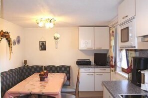 Compact living space with a kitchenette and dining area, featuring a table, bench, microwave, stove, sink, and refrigerator.