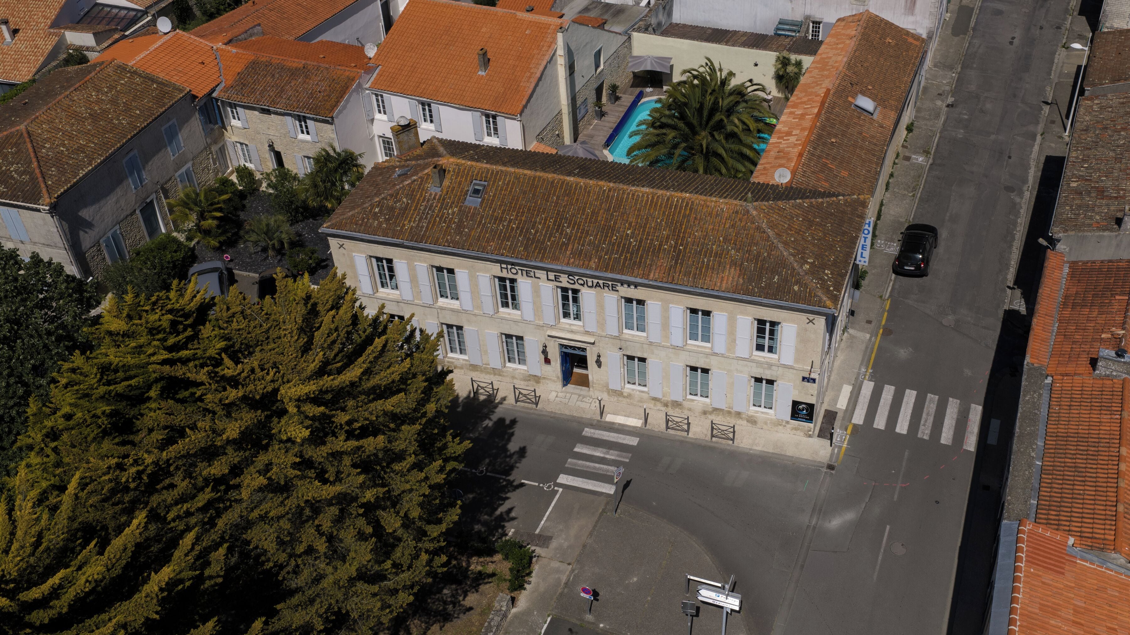 Un hotel con tetto in tegole, piscina e un attraversamento pedonale di fronte.