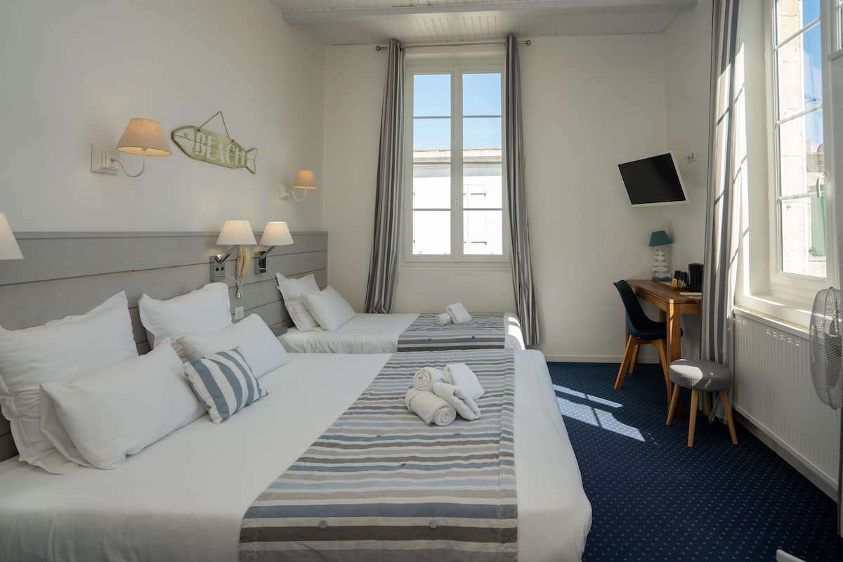 A hotel room with two beds, a desk, a chair, a TV, and a window with curtains.