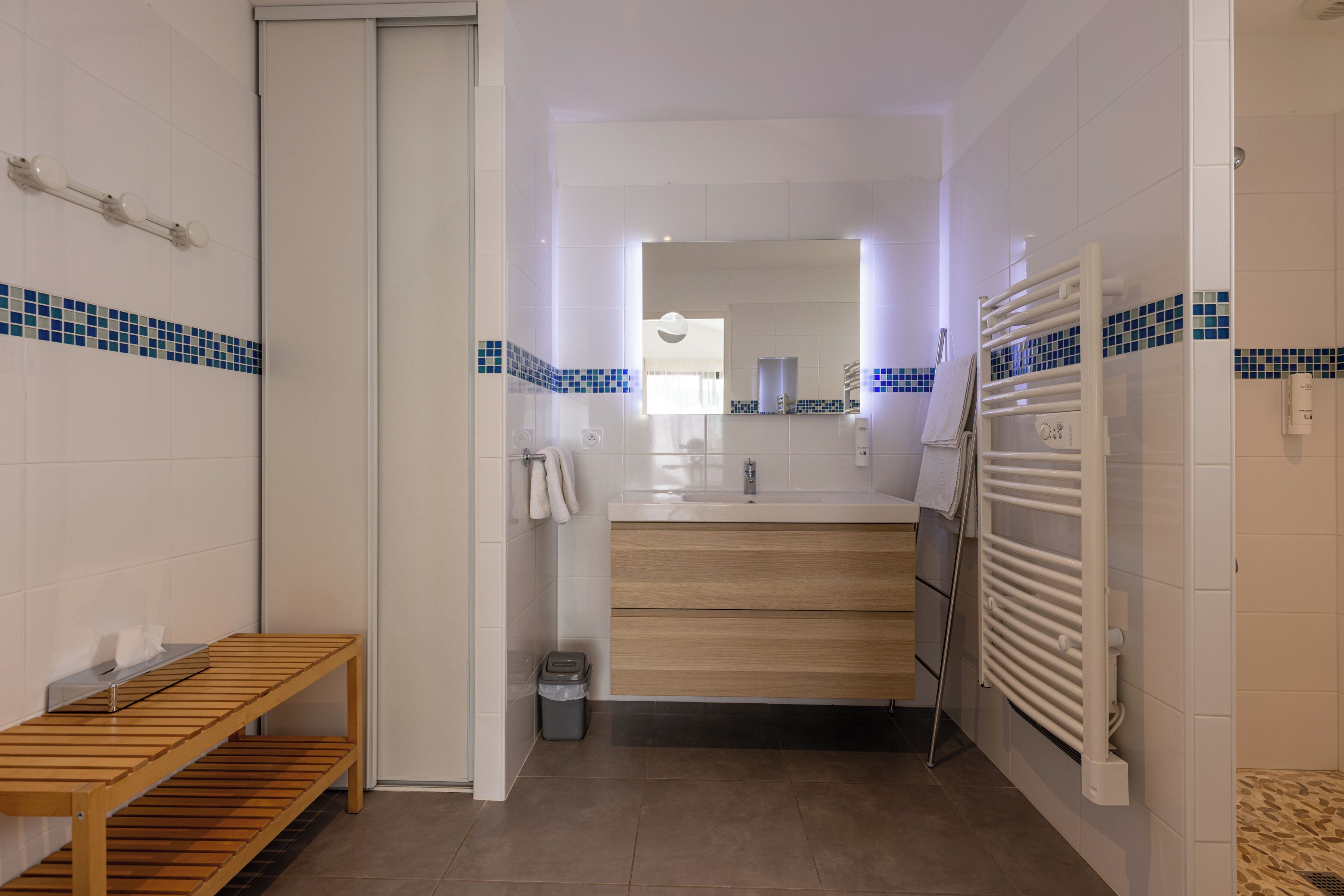 Un baño con un banco de madera, un lavamanos y un perchero para toallas.