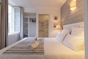 A hotel room with a large bed, a walk-in closet, a bathroom with a mirror, and a window with curtains. - Hotel Le Square (Saint-Pierre-d'Oleron)