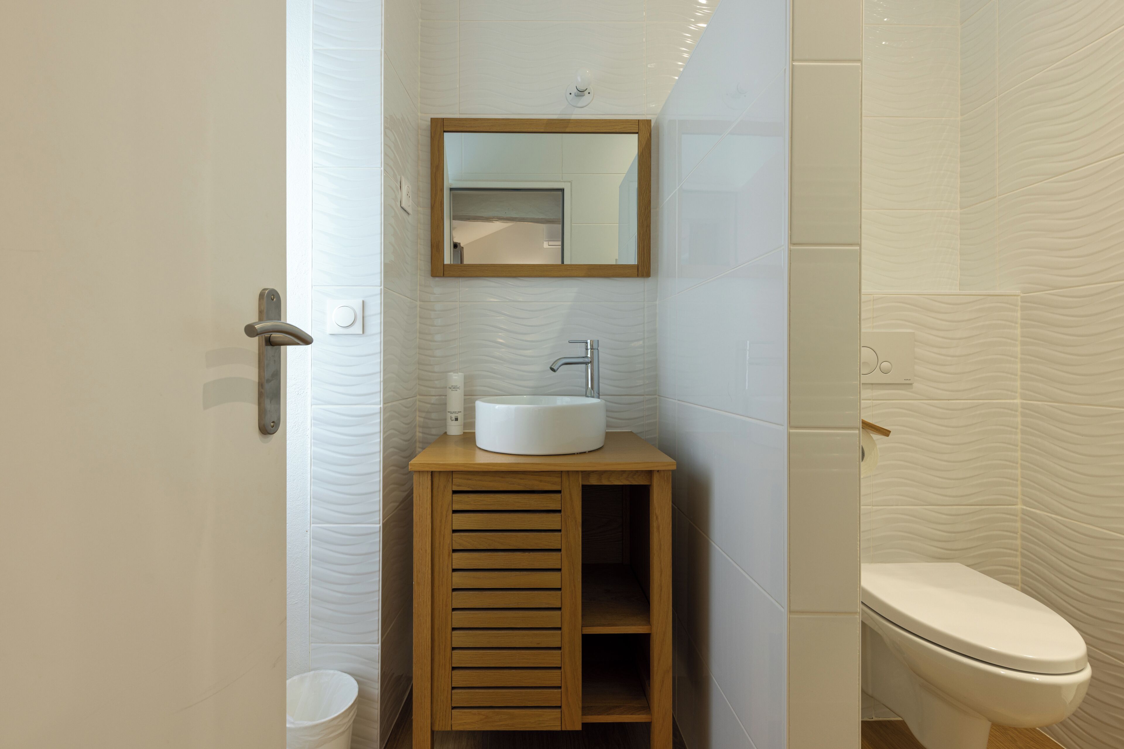 A bathroom with a wooden vanity, a white sink, a mirror, and a toilet.