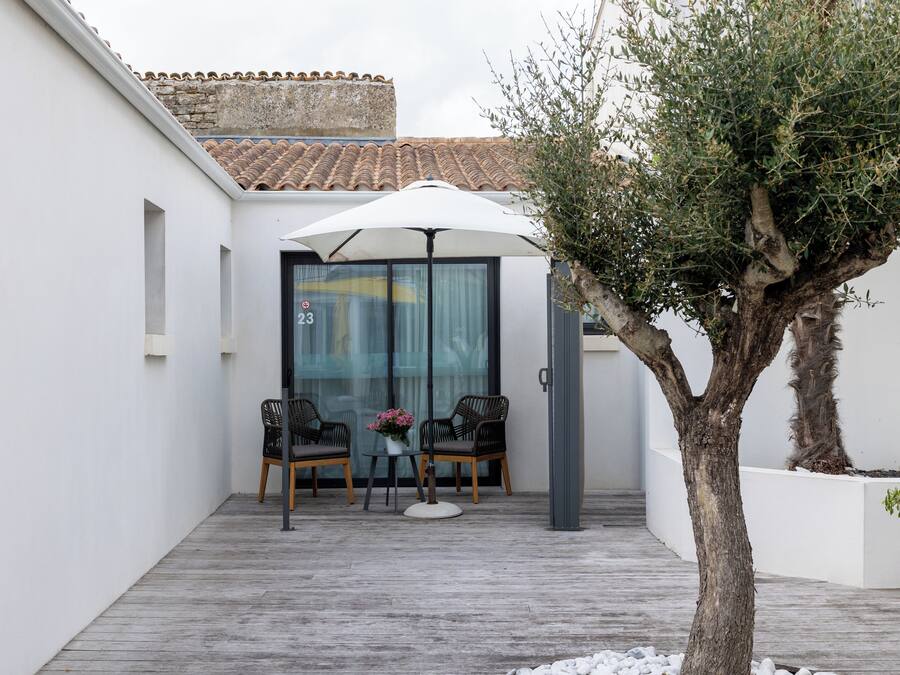 A patio with two chairs and a table, an umbrella, and a tree.