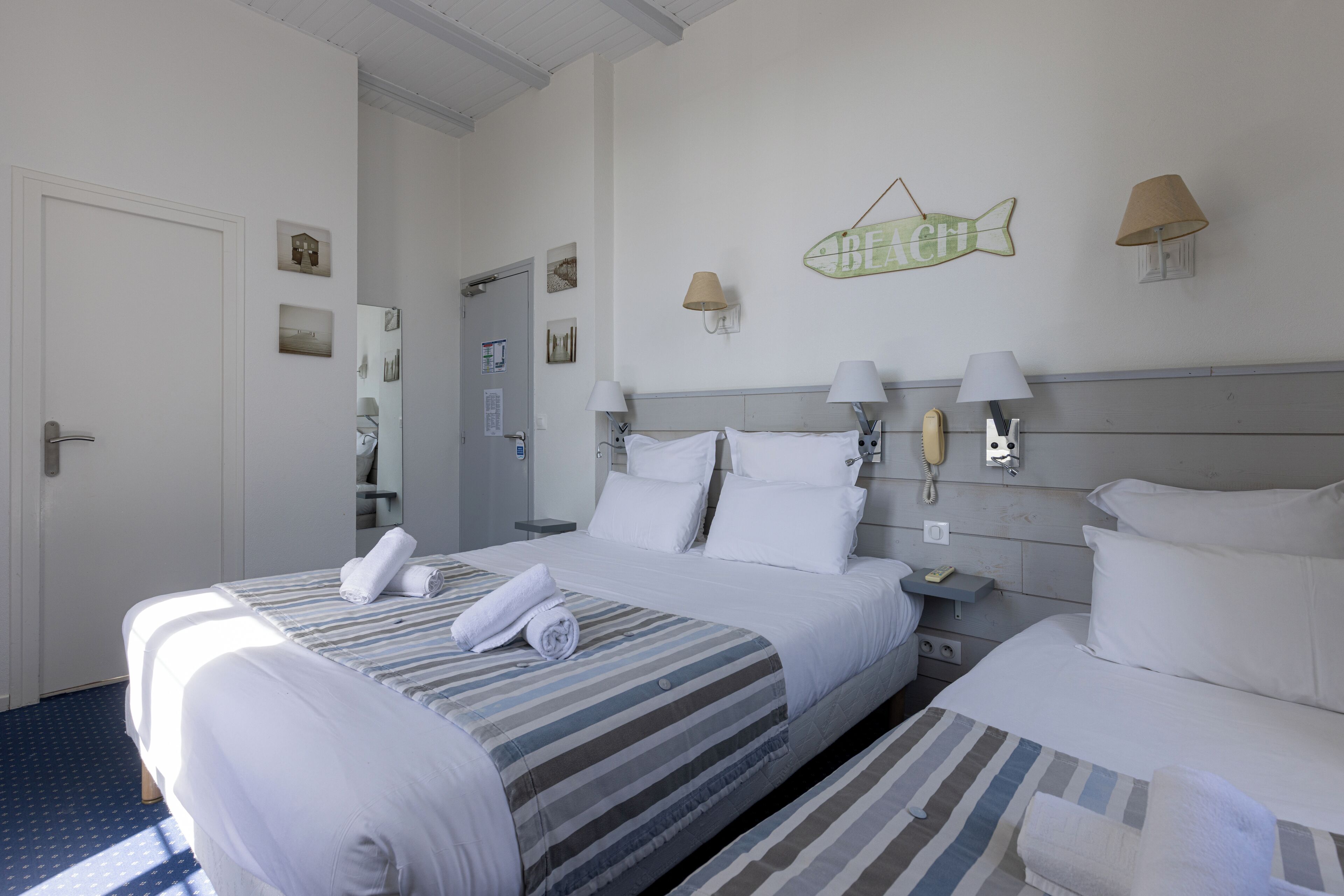 A hotel room with two beds, a small desk, a telephone, and a fish-shaped decoration on the wall.
