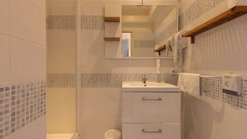Une salle de bain avec une douche à parois de verre, un lavabo avec un miroir au-dessus et un distributeur de serviettes.
