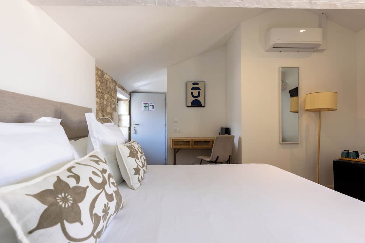 A hotel room with a bed, a desk, a chair, an air conditioner, and a mirror.