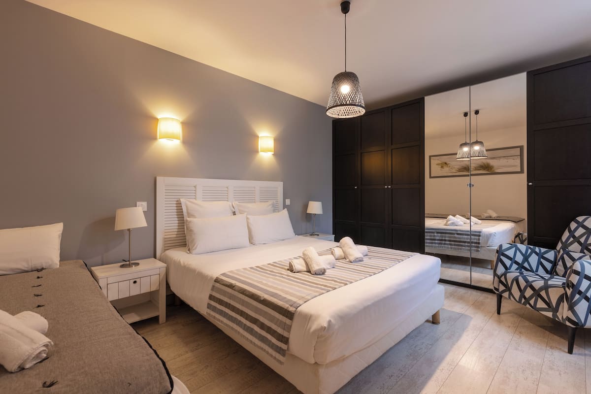 A modern hotel bedroom with a large bed, bedside tables, a chair, and a wardrobe.