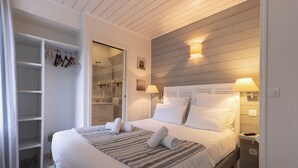 A neatly arranged bedroom with a large bed, a walk-in closet, and a wooden ceiling. - Hotel Le Square (Saint-Pierre-d'Oleron)