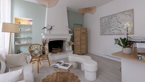 A modern living room with a fireplace, wicker furniture, and a bookshelf. - Hotel Le Square (Saint-Pierre-d'Oleron)