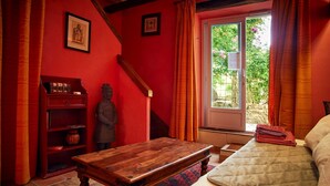 Een kamer met een bed, een houten tafel, een beeld, een boekenkast en een raam met gordijnen.