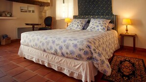 Een slaapkamer met een groot bed, twee bedlampen, een stoel, een klein tafeltje en een kamerbreed tapijt met een patroon.