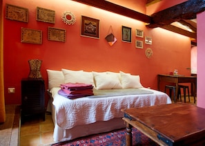 Une chambre à coucher avec un lit, des oreillers, une table de chevet, une table en bois et un mur orné de tableaux.