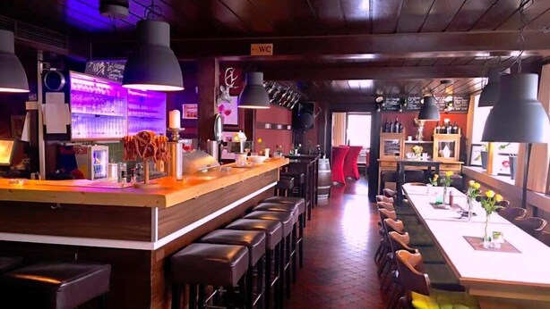 Un espace bar doté d’un long comptoir, de tabourets et d’un coin salon avec des tables et des chaises.