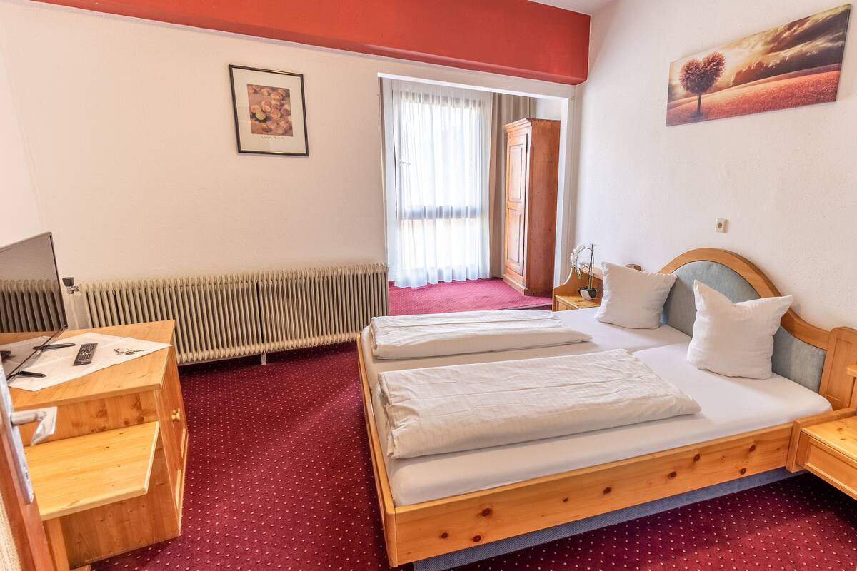 Ein Hotelzimmer mit zwei Betten, einem Schreibtisch, einem Heizkörper und einem Fenster mit Vorhängen.