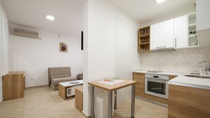 A modern kitchen with a built-in oven, a dining table, and a sofa in the adjacent living area. - Apartmani Mia (Sveti Stefan)