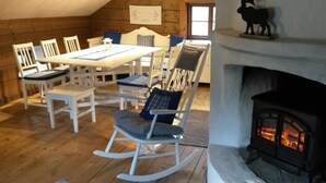 A cozy room with a fireplace, wooden flooring, white furniture, and a dining table. - STF Långasjö Vandrarhem (Långasjö)