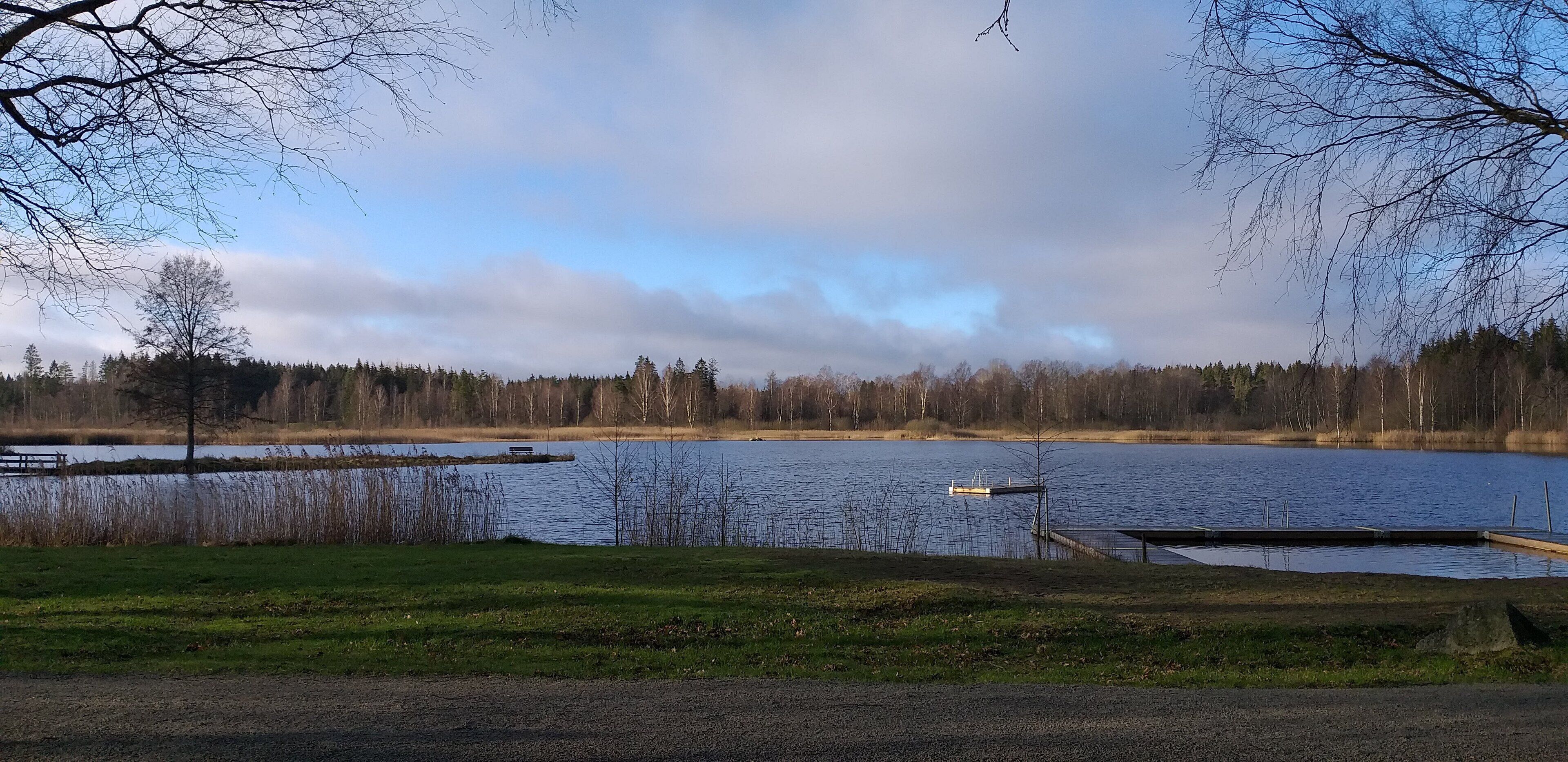 A serene lakeside view with a dock, grassy area, and trees in the background.