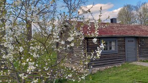 A rustic log cabin with a red roof, surrounded by blooming trees and a clear sky. - STF Långasjö Vandrarhem (Långasjö)