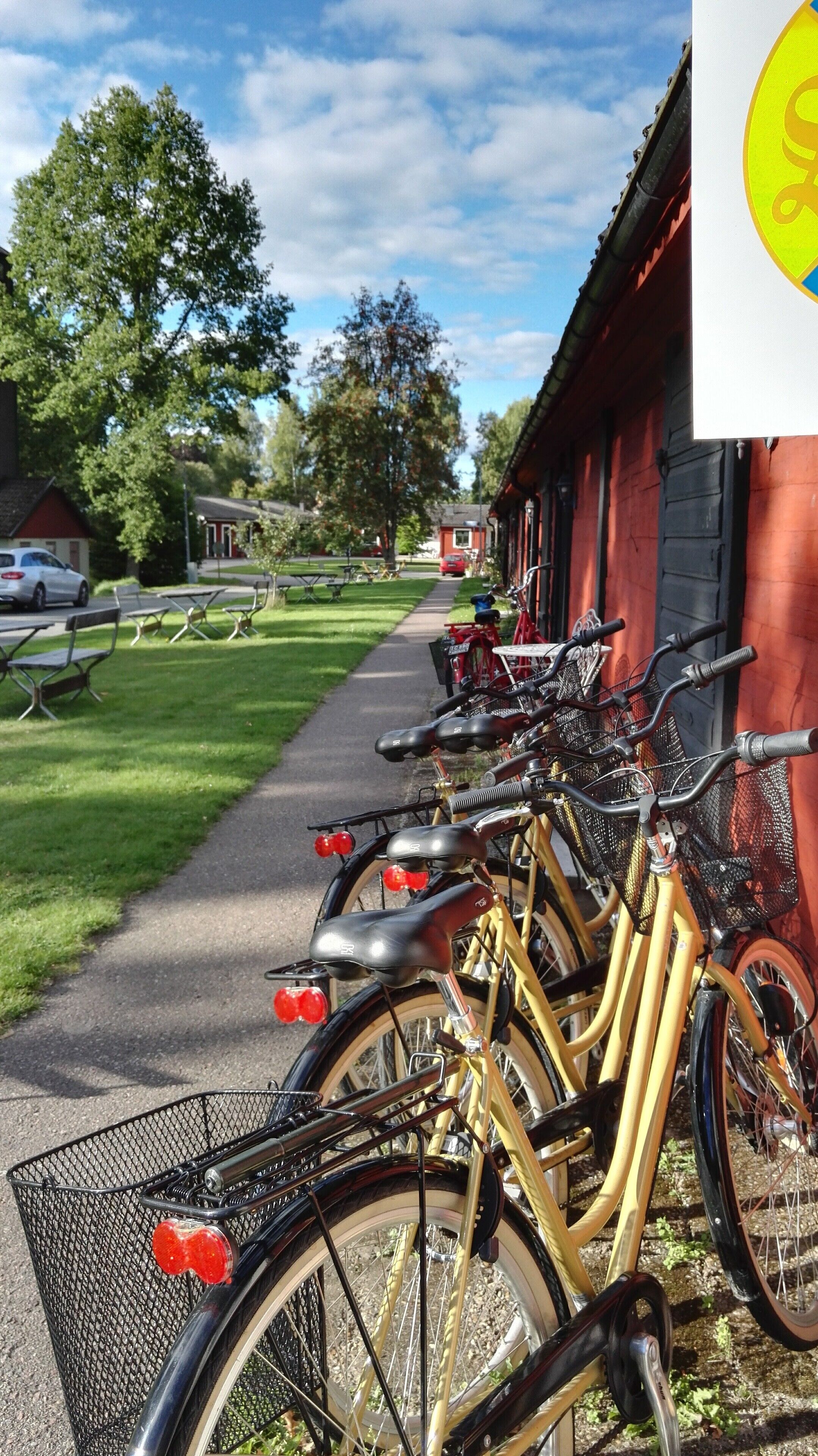 Une rangée de vélos est stationnée sur un trottoir, à côté d’un bâtiment rouge.