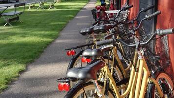 Une rangée de vélos est stationnée sur un trottoir, à côté d’un bâtiment rouge.