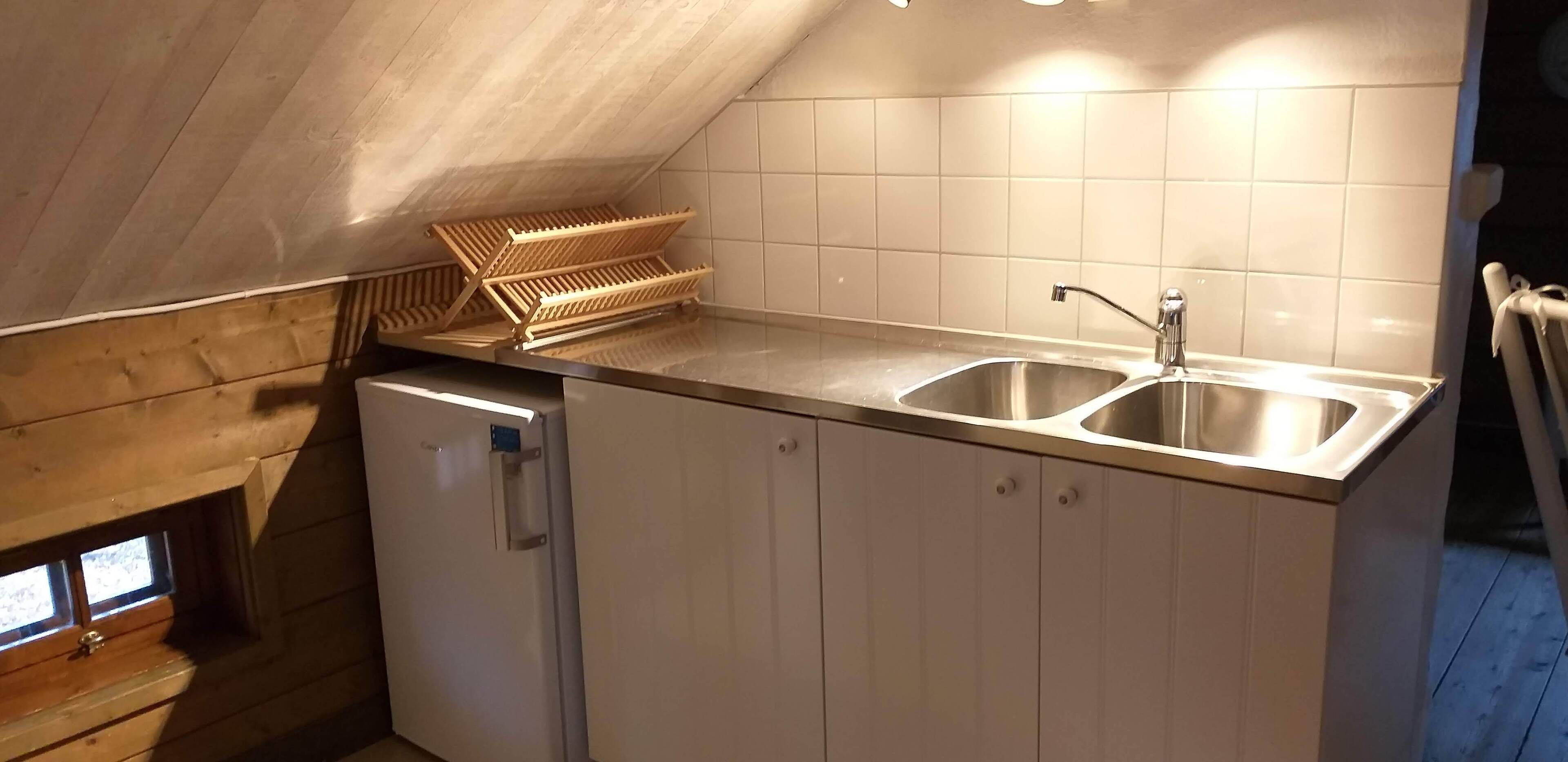 A compact kitchen with a double sink, wooden cabinets, and a small refrigerator.