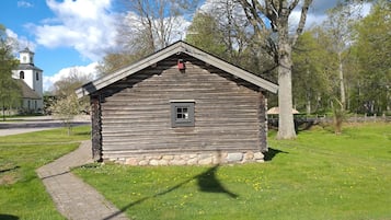 A rustic wooden cabin with a small window, surrounded by a grassy area and trees.