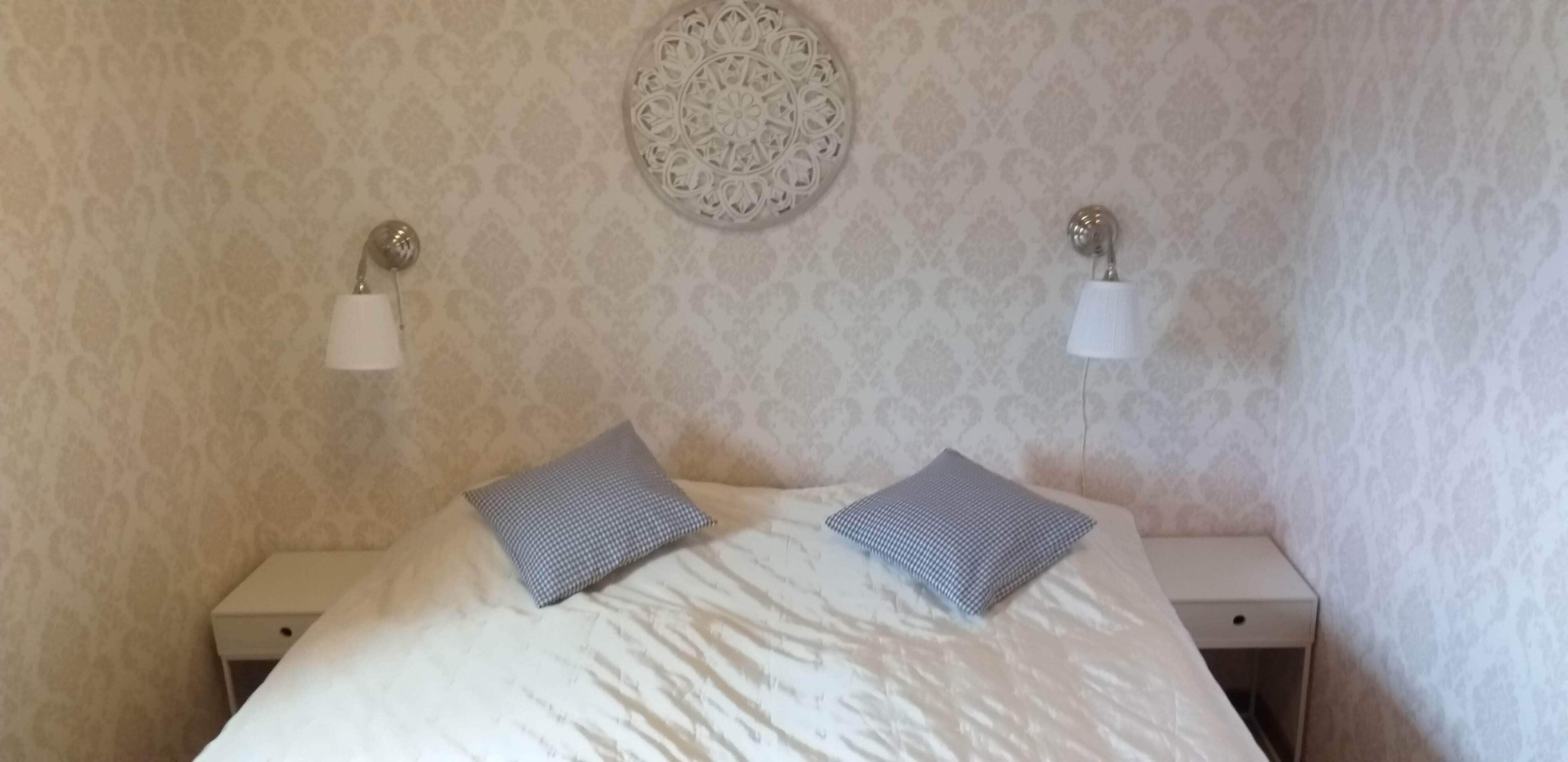 A neatly made bed with two pillows, a wall-mounted decorative plate, and two bedside lamps on a nightstand.