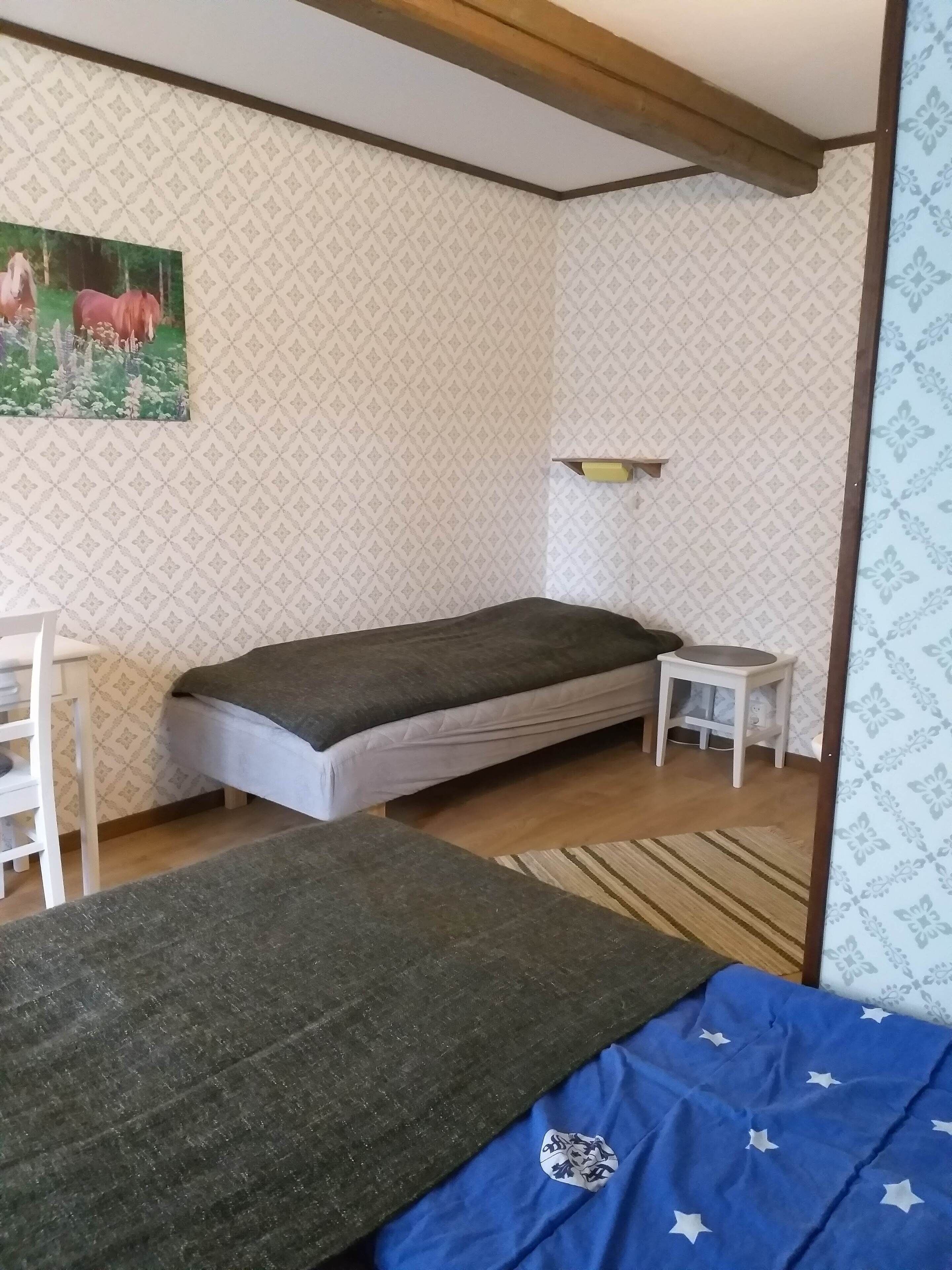 A room with a bed, a small table, a shelf, and a painting on the wall.