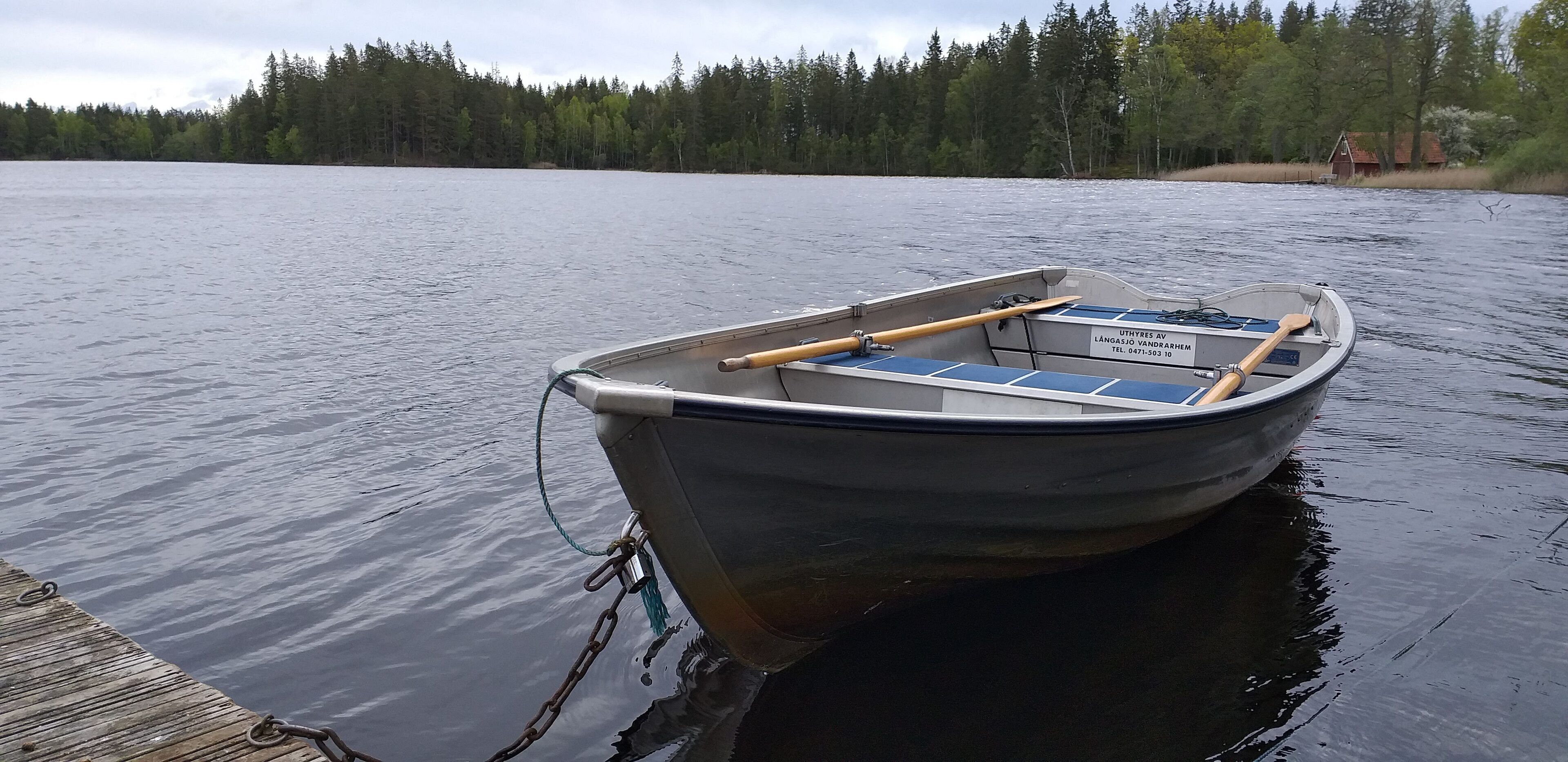 A small motorboat docked at a wooden pier with a forested shoreline in the background.