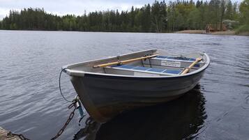 A small motorboat docked at a wooden pier with a forested shoreline in the background.