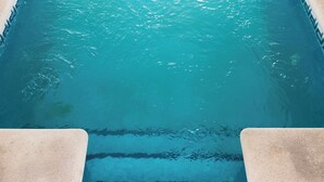 A swimming pool with clear blue water, tiled steps leading into the pool, and a tiled floor around the pool area.